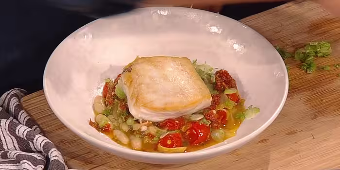 Hake with fennel and sun-dried tomatoes in cream bowl on a wooden worktop